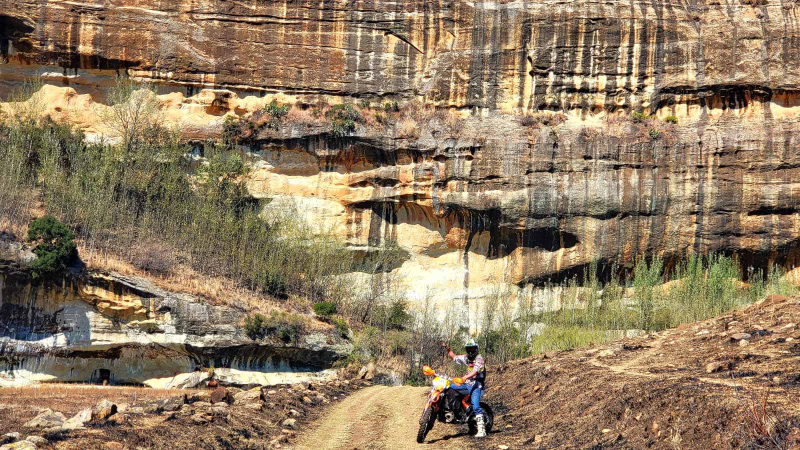 A rider on a two-track trail below a banded sandstone cliff at Glen Lyon.